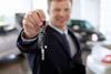 150753 Waist up photograph of smiling car salesman looking at camera, holding out car key, focus on car key and hand in foreground