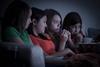 151521 Four female teenage friends watching scary film on sofa with popcorn