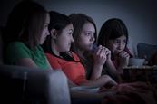 151521 Four female teenage friends watching scary film on sofa with popcorn