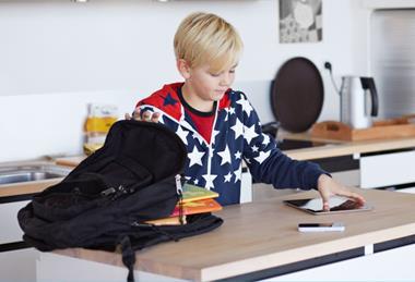 Boy putting his school supplies into his backpack