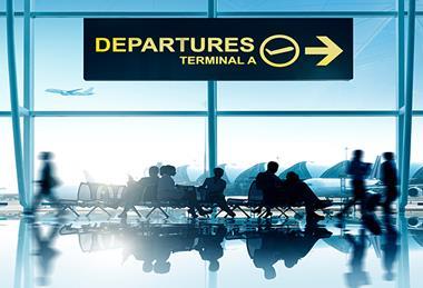 140503 Departures lounge with people waiting on benches at an airport with planes flying in background, seen through glass wall.