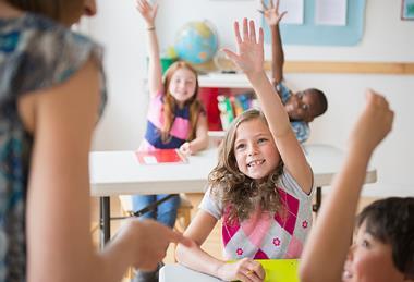 Photo of a teacher talking to their students in a classroom. (students should be children)