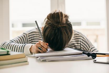 Photo of a student who's visibly struggling to write a text. Can be in a classroom or library environment.