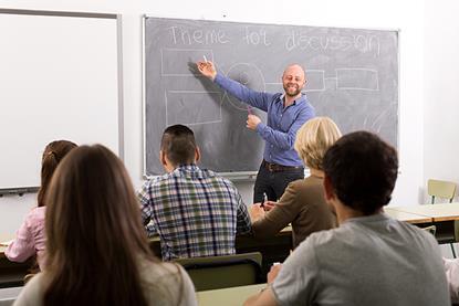 Photo of a class where the teacher is explaining somethig and students are shown to listen and follow.