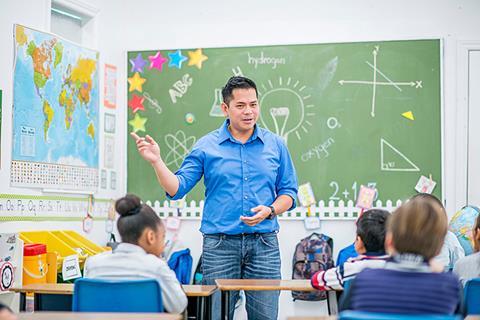 Photo of a teacher and their young students  together in a classroom. Ideally, the teacher  is speaking or writing something on the board.